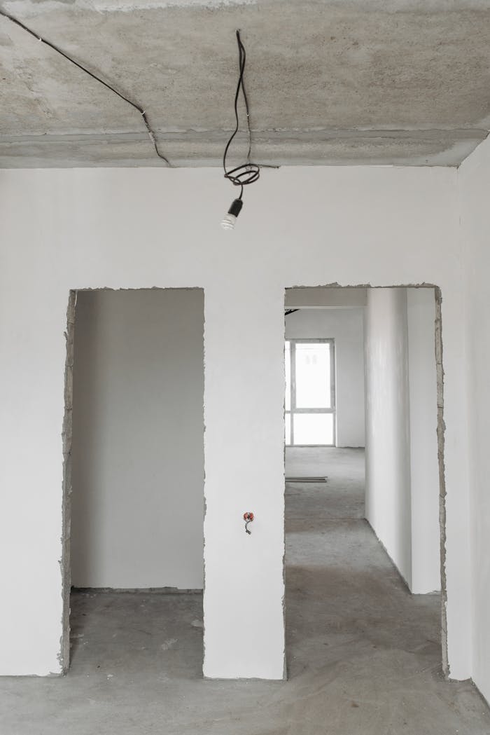 portfolio-06 Unfinished room interior with white plastered walls and exposed ceiling in a construction site.