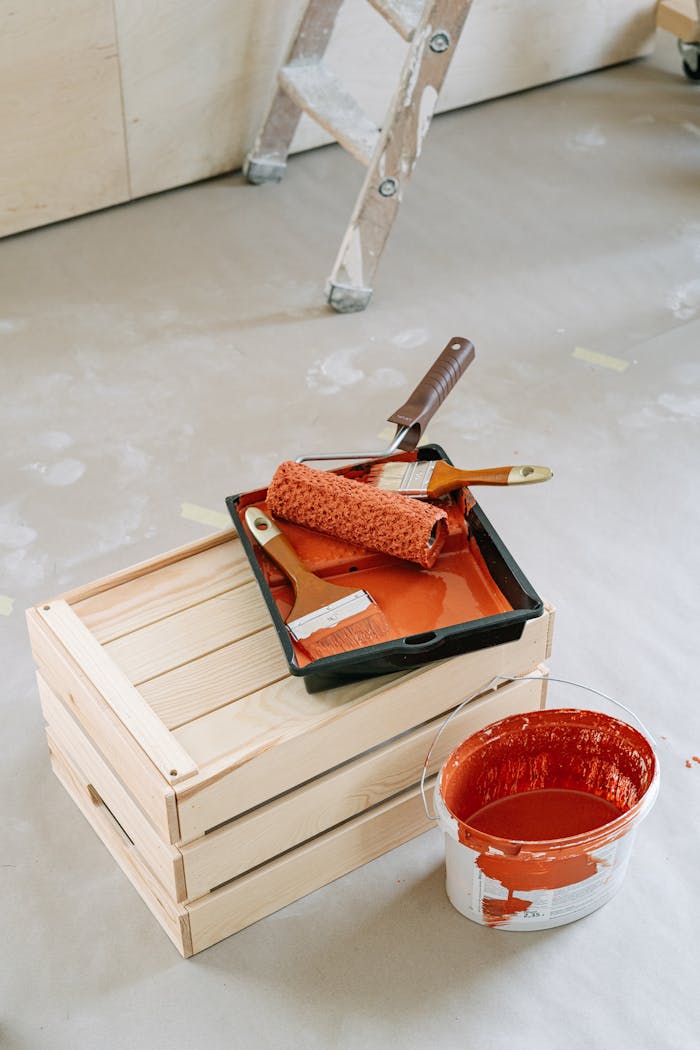 why-choose-us A close-up of home renovation tools including paint roller and red paint bucket on a wooden crate.