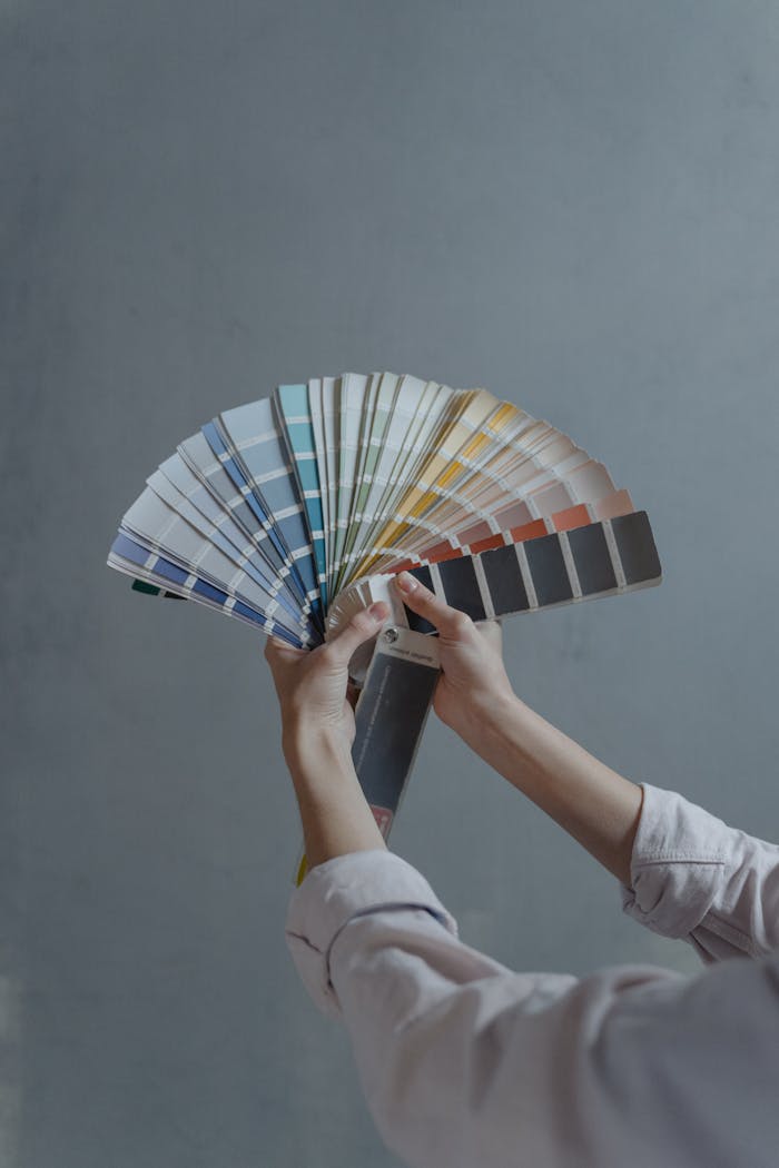 portfolio-02 Hands displaying a fan of paint color swatches against a gray wall, ideal for home renovation projects.