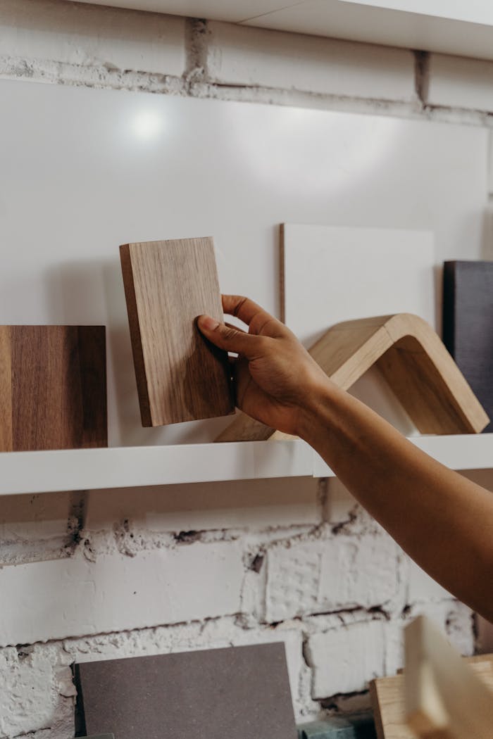 stats-img A hand picks up a wooden sample from a shelf with various design elements, highlighting interior choices.